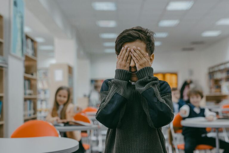 boy in black and gray sweater covering his eyes with his hands